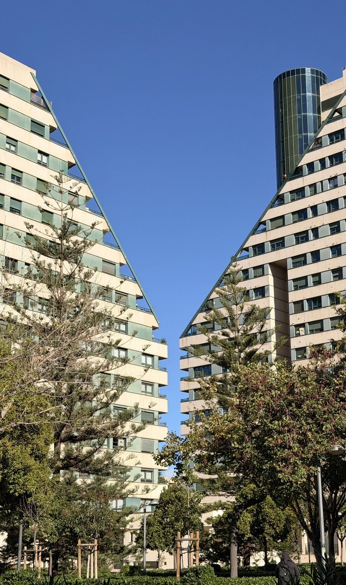 Dos edificios de forma triangular enfrentados, con una franja de cielo azul entre ambos y árboles al pie